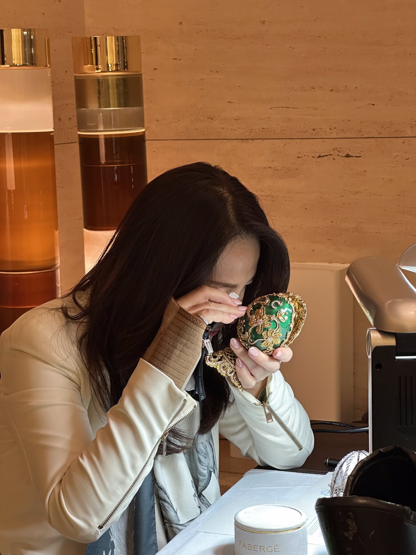 Kehan Li holding a green and gold Faberg&eacute; egg up to her loupe, examining it at close range.